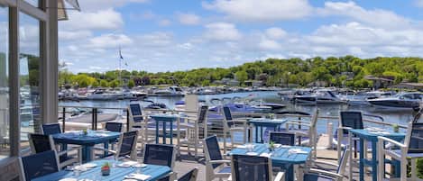 Un espacio de comedor al aire libre con mesas y sillas, con vista a un puerto deportivo lleno de barcos.