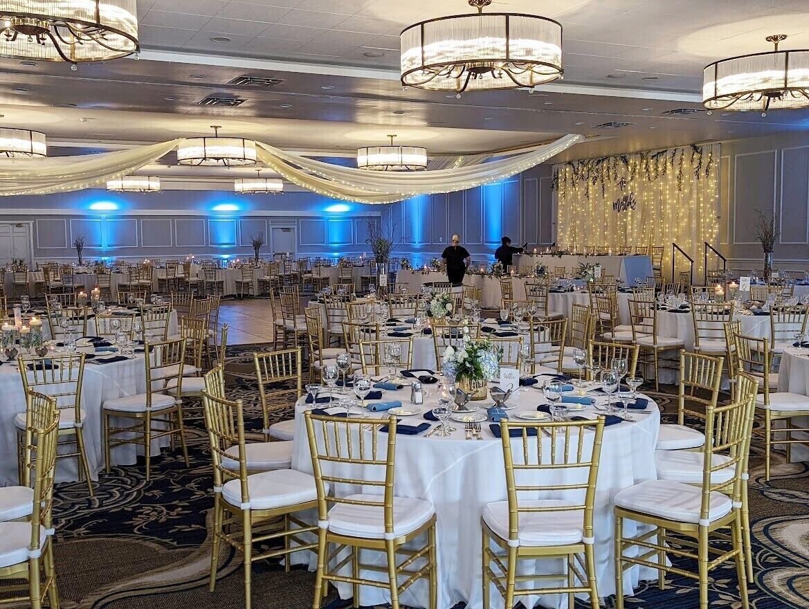 A banquet hall with round tables set for a formal event, featuring gold chairs and white tablecloths.