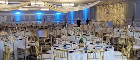 A banquet hall with round tables set for a formal event, featuring gold chairs and white tablecloths.
