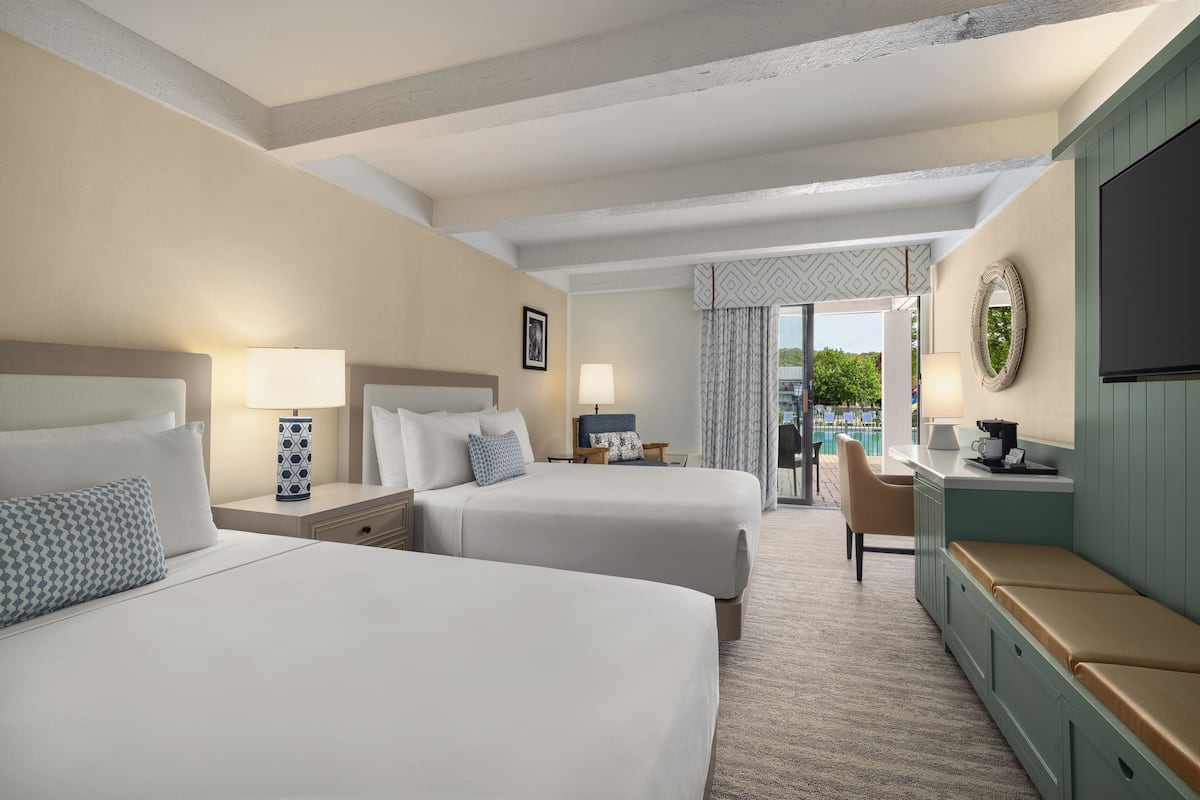 A hotel room with two beds, a TV, a desk with a chair, and a view of the outdoors.
