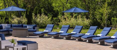A patio area with lounge chairs and umbrellas, surrounded by greenery.