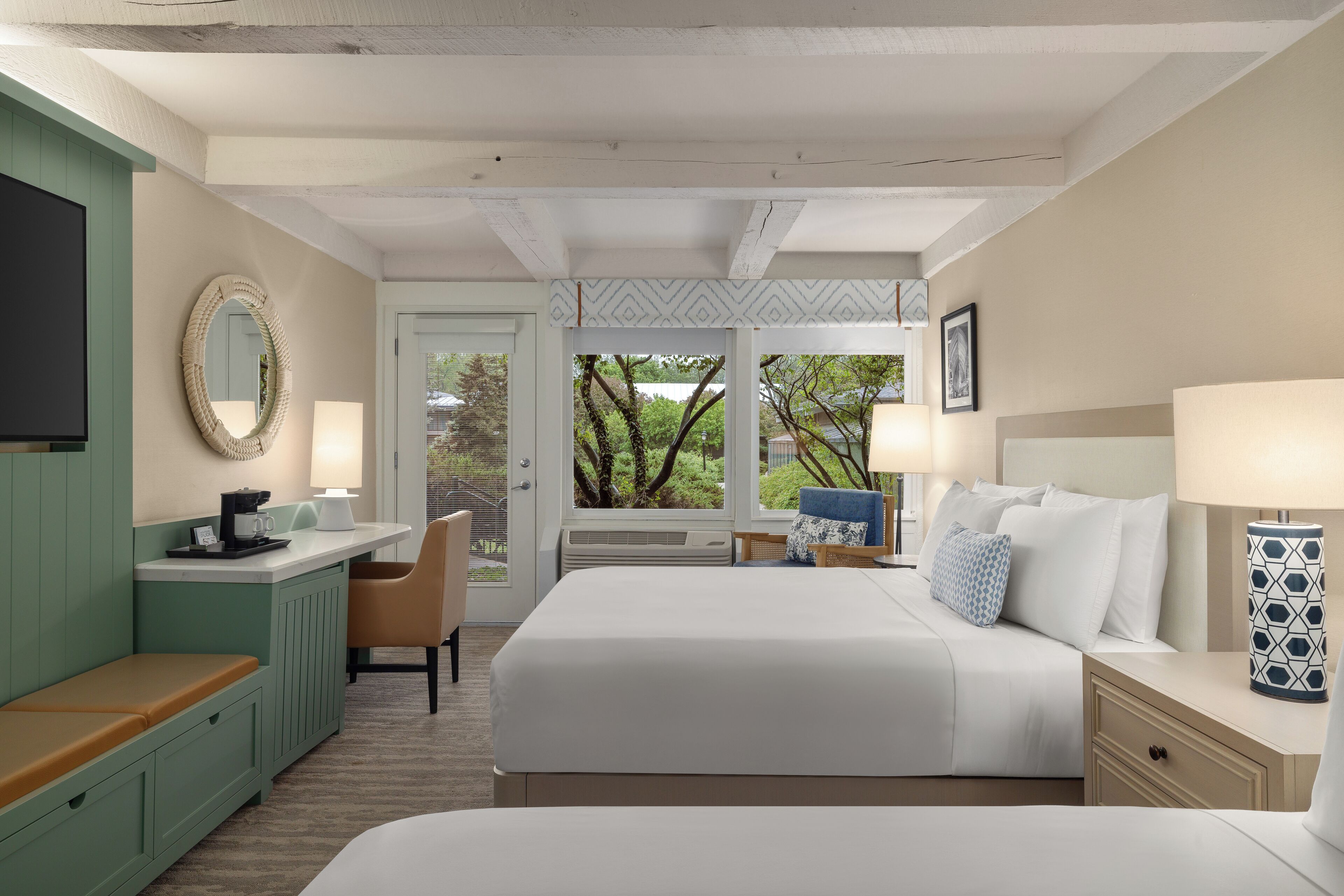 Une chambre d’hôtel avec un lit, des tables de chevet, un bureau avec une chaise, une télévision et une vue sur les arbres par la fenêtre.
