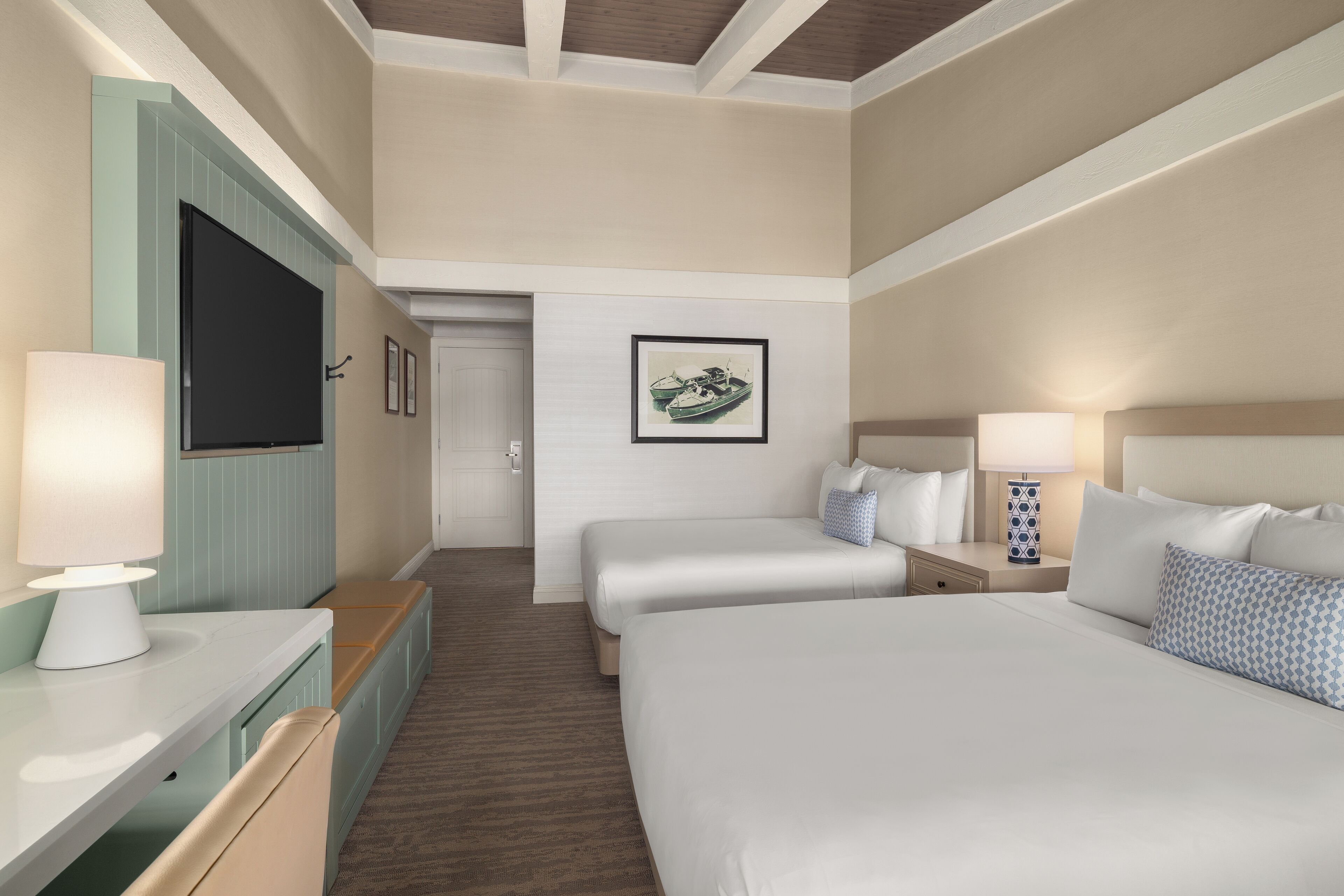 A hotel room with a large bed, two smaller beds, a TV, a desk with a lamp, and a framed picture on the wall.