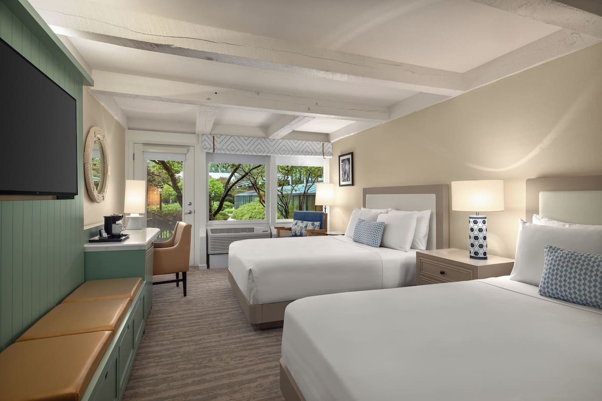A hotel room with two beds, a desk, a chair, and a TV.