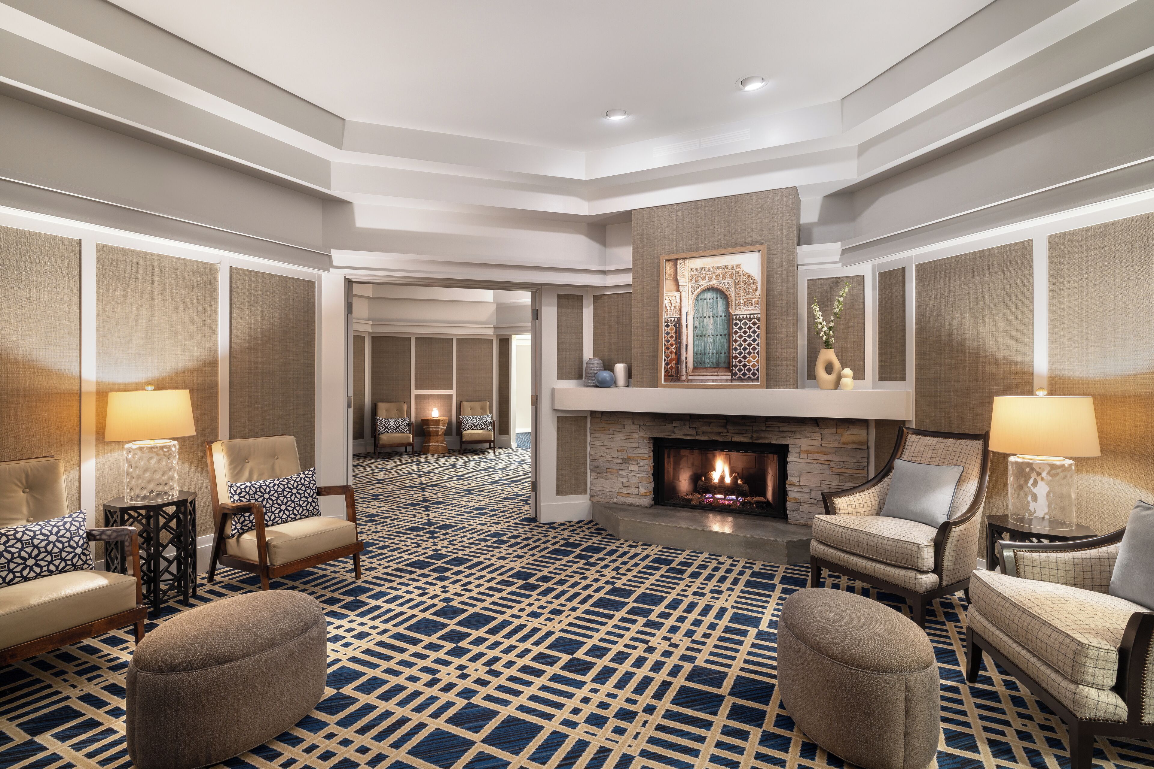 A spacious lobby with a patterned carpet, multiple seating areas, a fireplace, and a decorative wall piece.