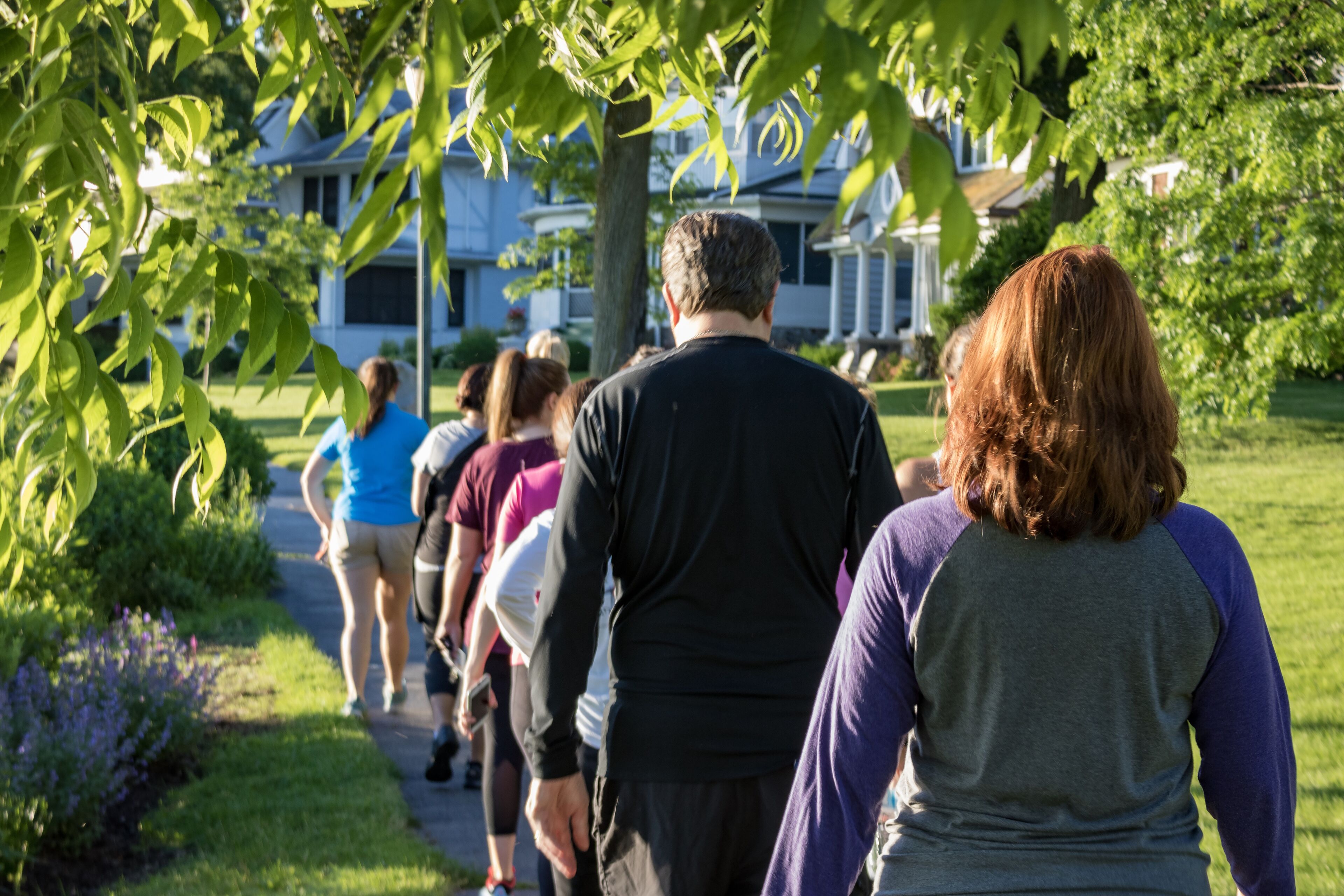 Un grupo de personas caminando por un sendero en una zona residencial con casas al fondo.