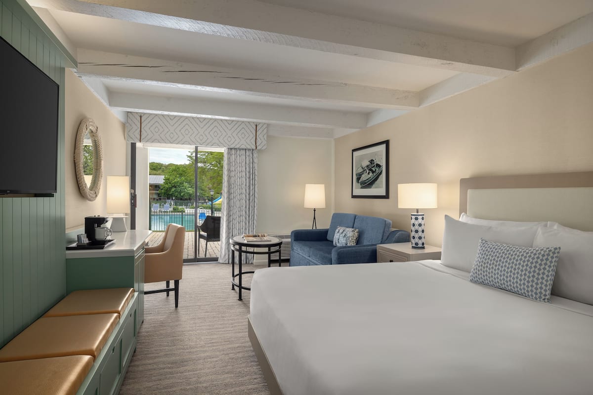 A hotel room with a large bed, a desk with a chair, a sofa, a small table, and a TV.