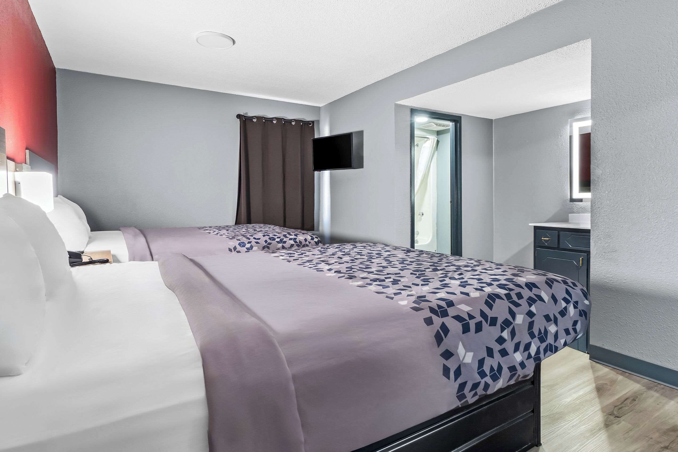 A hotel room with two beds, a TV, a shower, and a small desk.