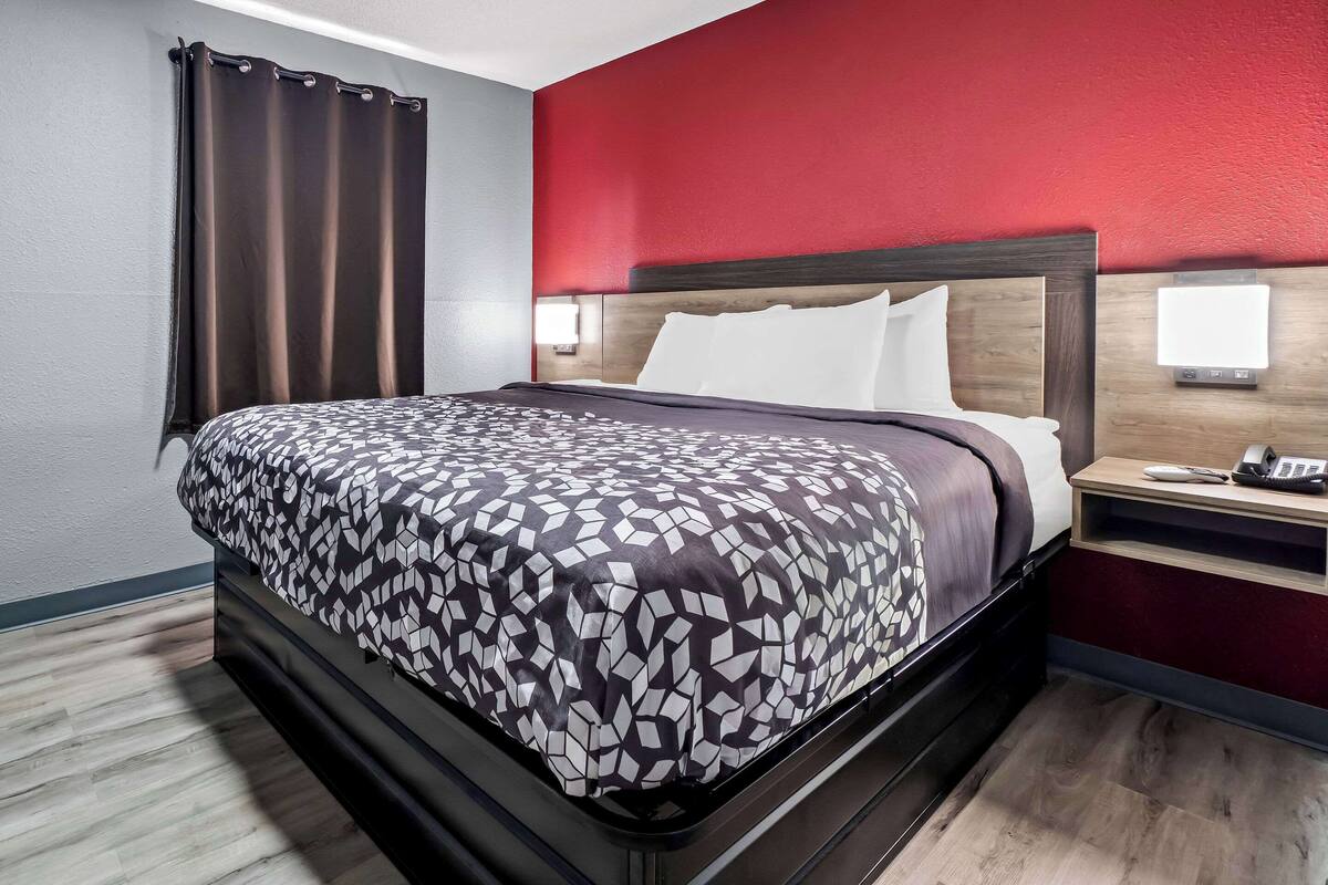A hotel room with a bed, a nightstand, and a red accent wall.