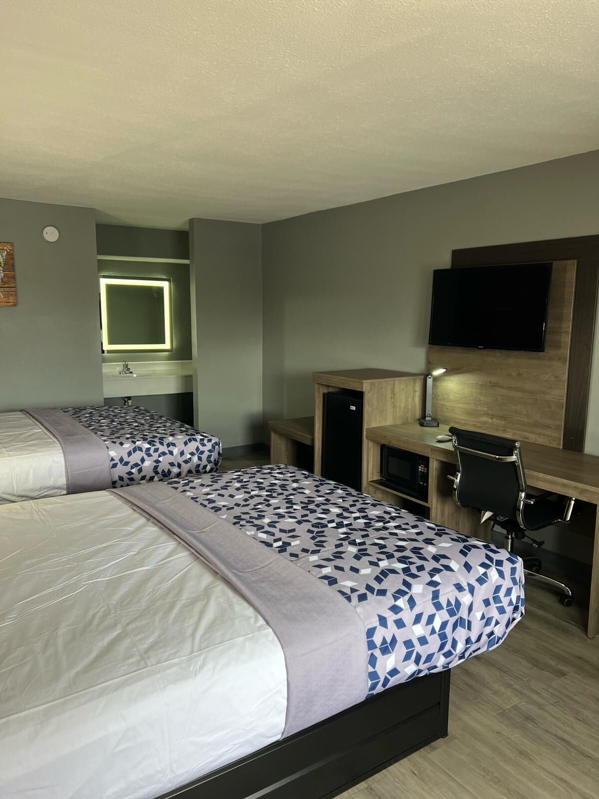 Ein Hotelzimmer mit zwei Betten, einem Schreibtisch, einem Fernseher und einem Spiegel.