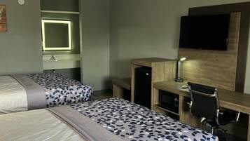 Ein Hotelzimmer mit zwei Betten, einem Schreibtisch, einem Fernseher und einem Spiegel.