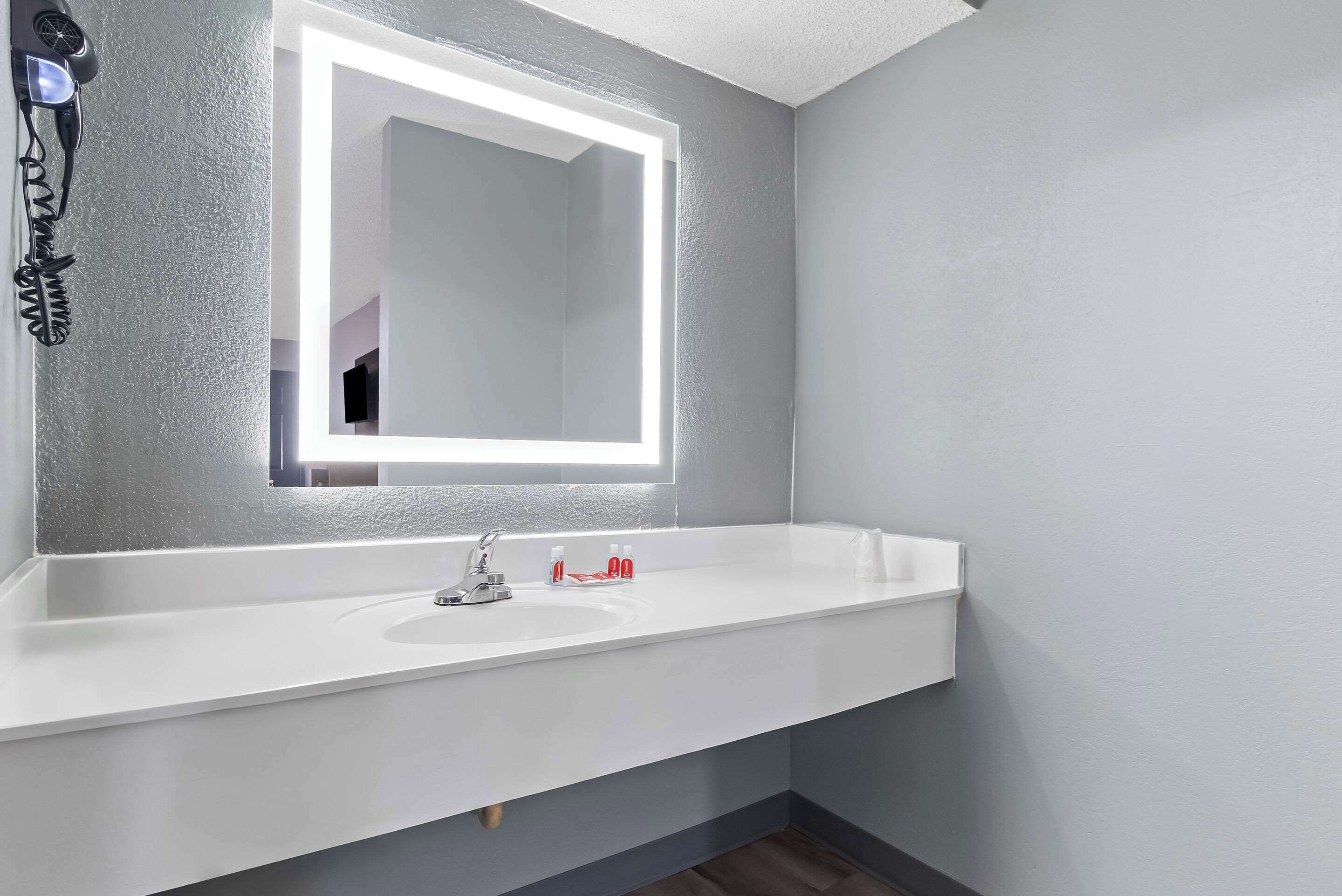 A bathroom with a white sink, a mirror with LED lighting, and a hairdryer on the wall.