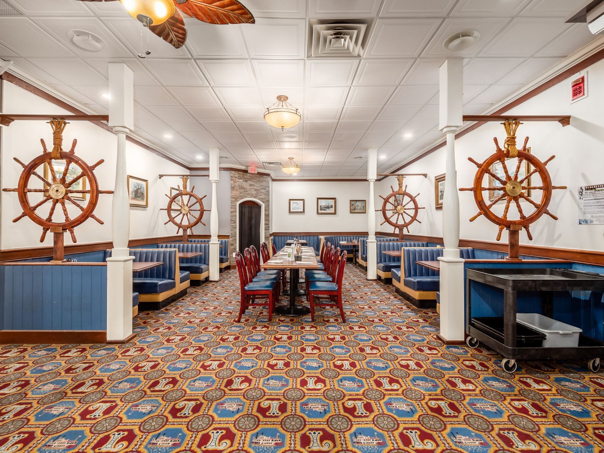 A nautical-themed restaurant with round wooden tables, blue cushioned booths, and a patterned floor.