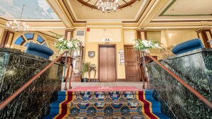 Una imponente escalera con un suelo estampado que lleva a una puerta, un candelabro y un diseño de techo con rosca de barco.