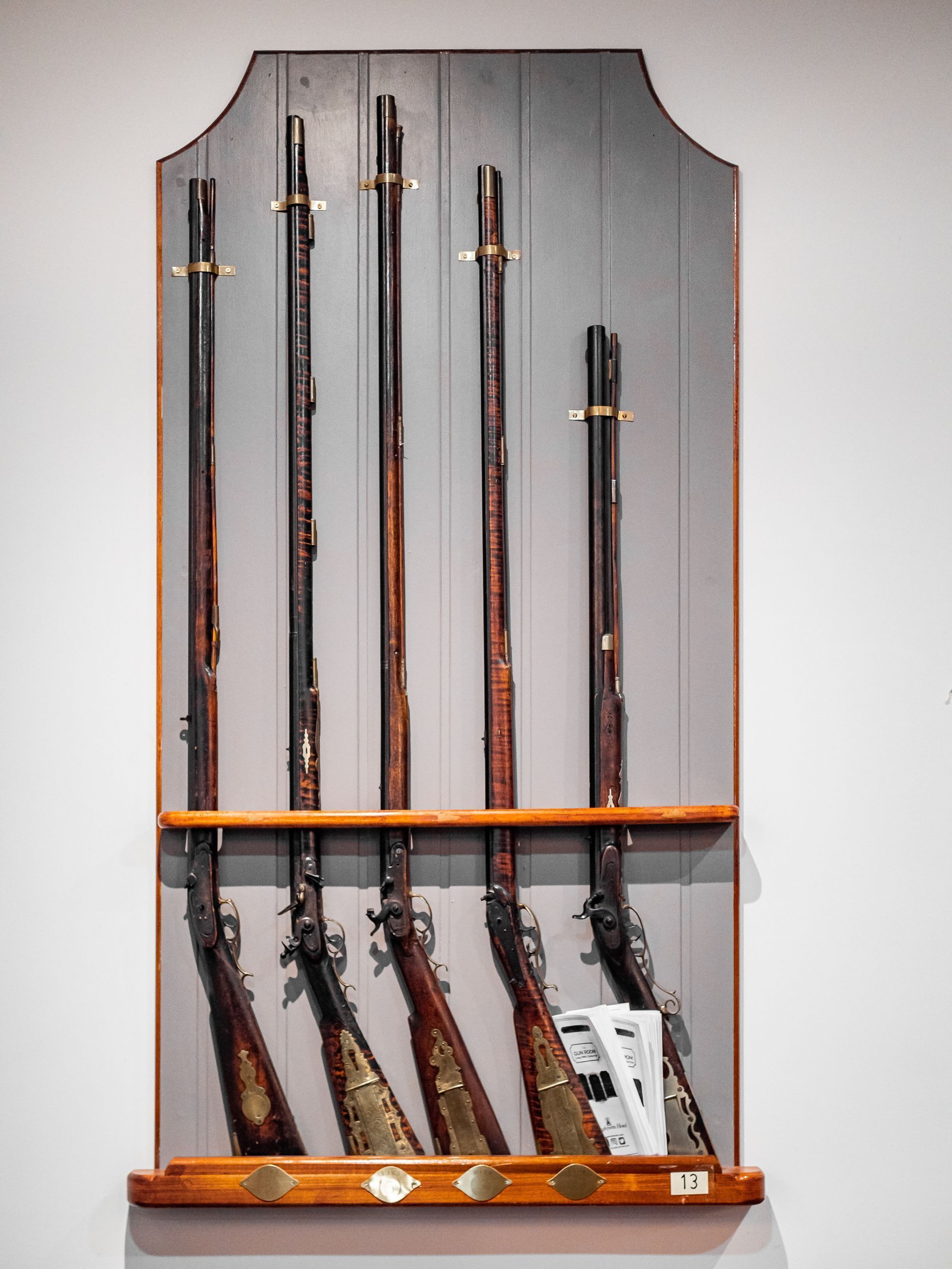 A wall-mounted rack with five long, dark wooden rifles and a handgun.