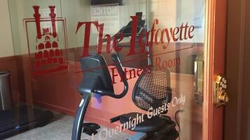 Une salle de remise en forme équipée d’un vélo d’appartement et d’un tapis de course, avec une porte vitrée sur laquelle est apposée une pancarte indiquant : « Salle de remise en forme Lafayette, réservée aux clients de l’hôtel qui y passent la nuit. »