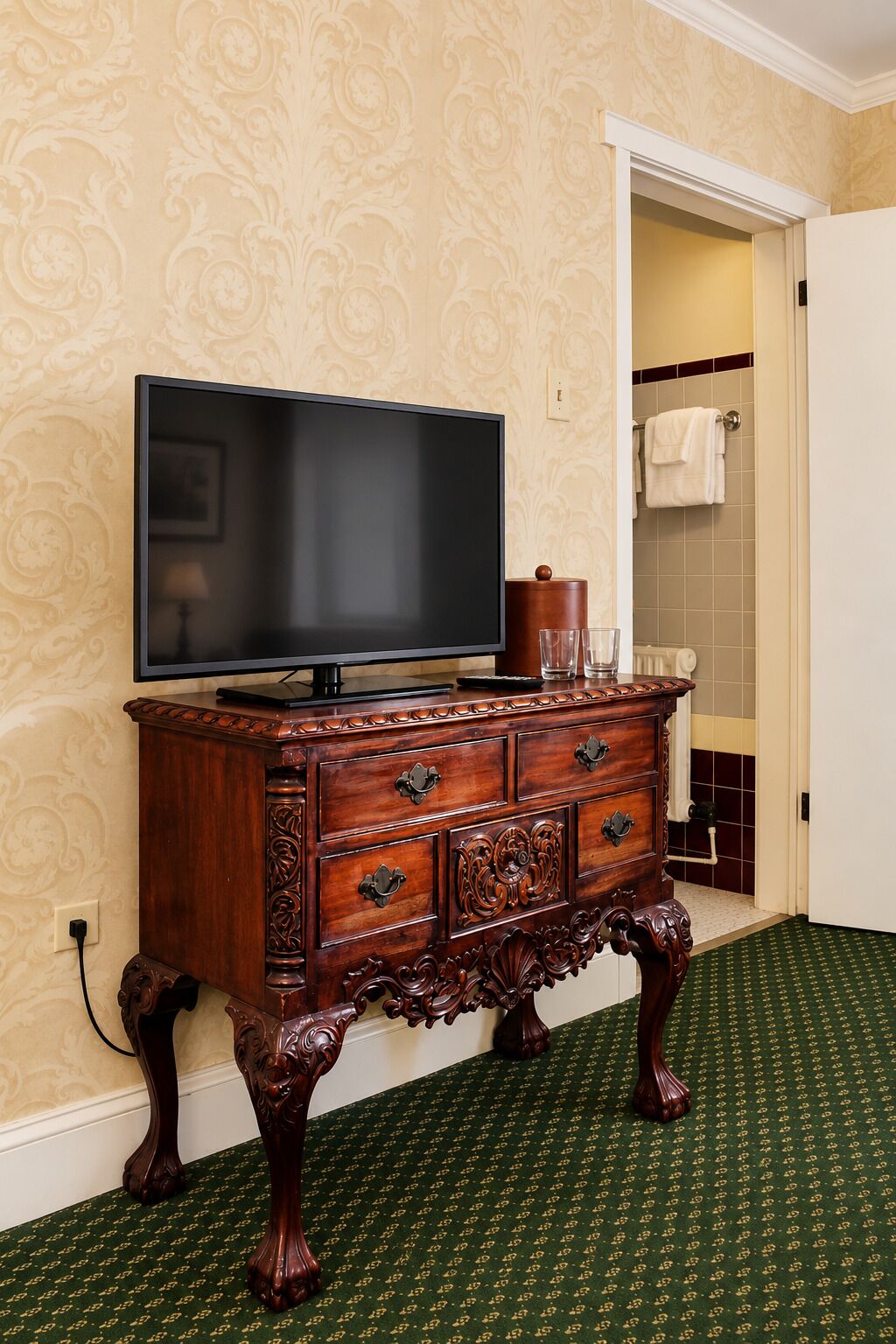 Un mueble de madera con un televisor encima, un baño con toallero y una alfombra estampada.