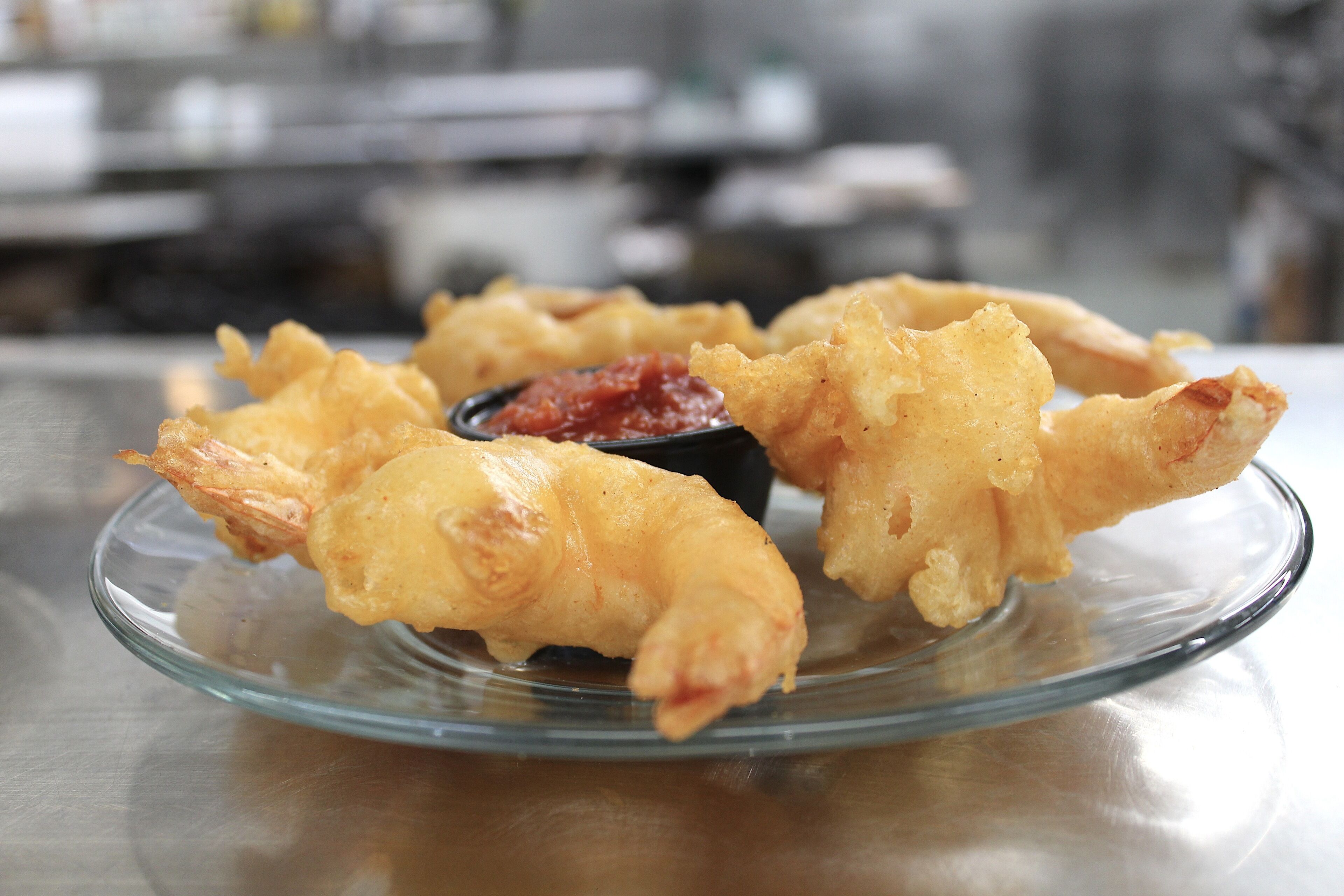 A glass plate with fried shrimp and a small bowl of dipping sauce.