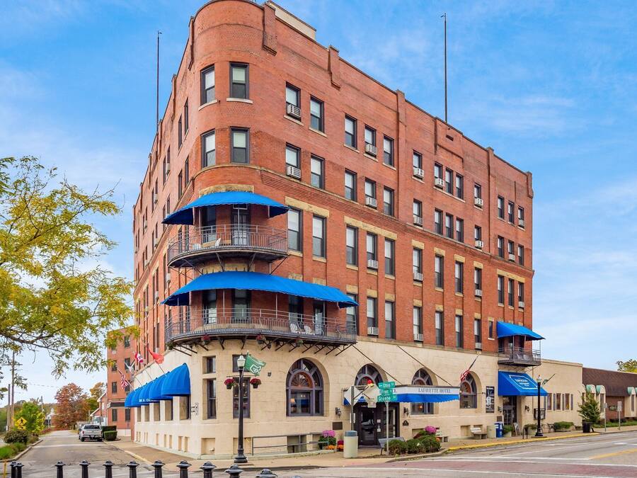 A multi-story brick building with a corner entrance, a balcony with blue awnings, and a sign for the Lafayette Hotel.