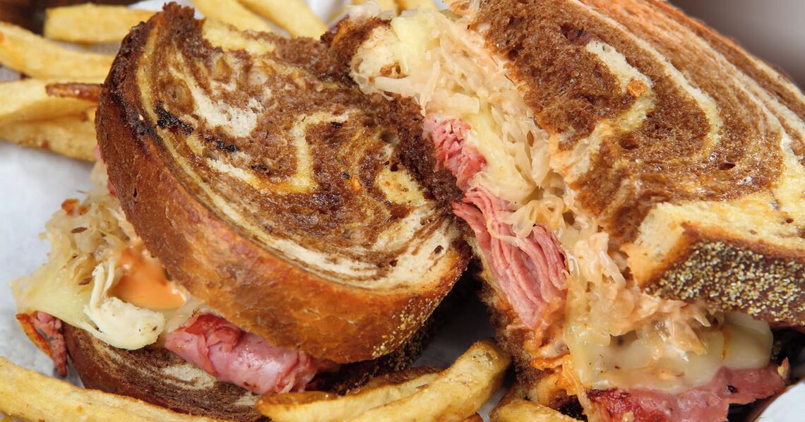 Un sándwich con queso derretido, jamón y chucrut entre rebanadas de pan tostado.