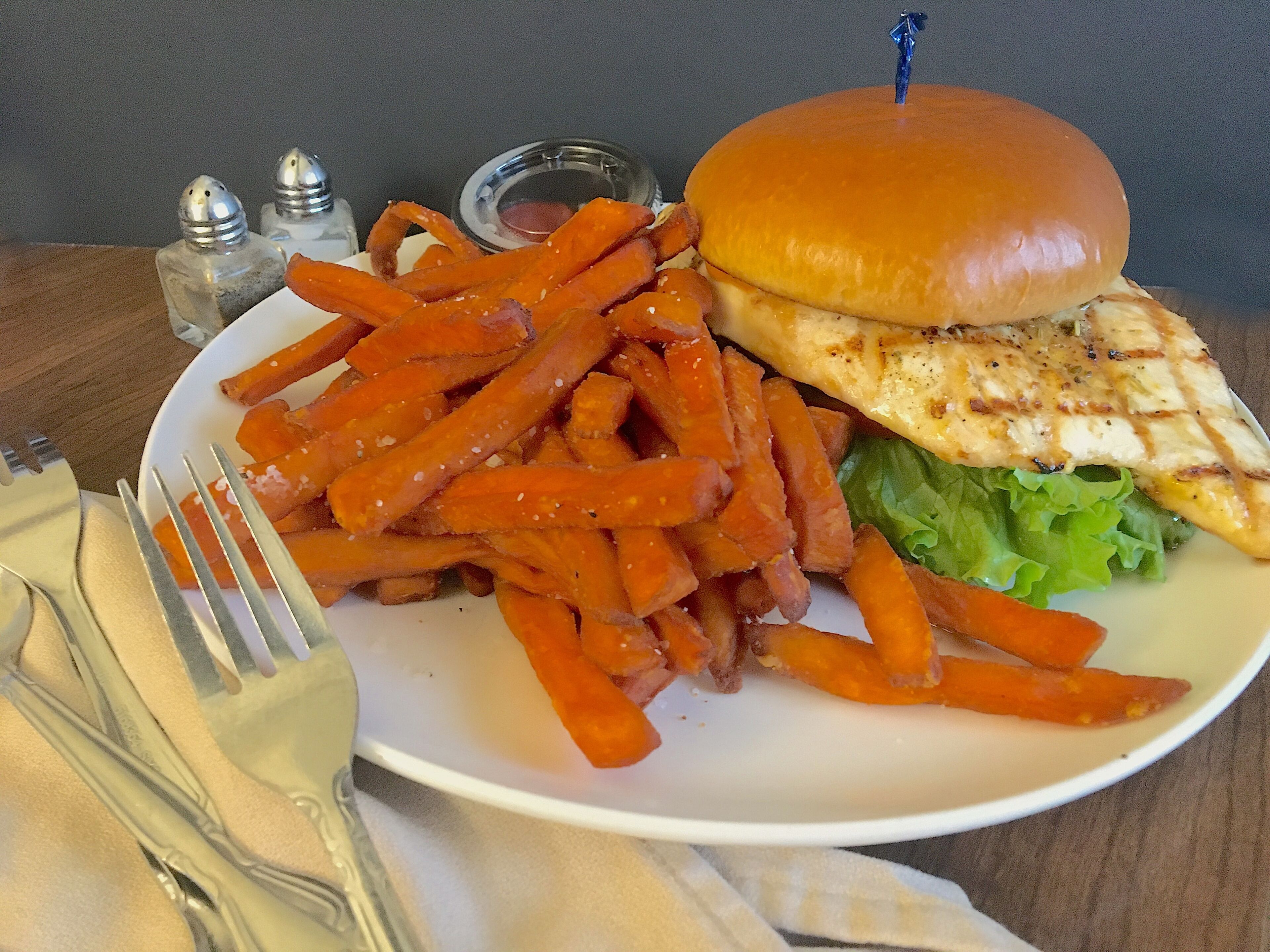 A plate with a grilled chicken sandwich, fries, and a small container of sauce.