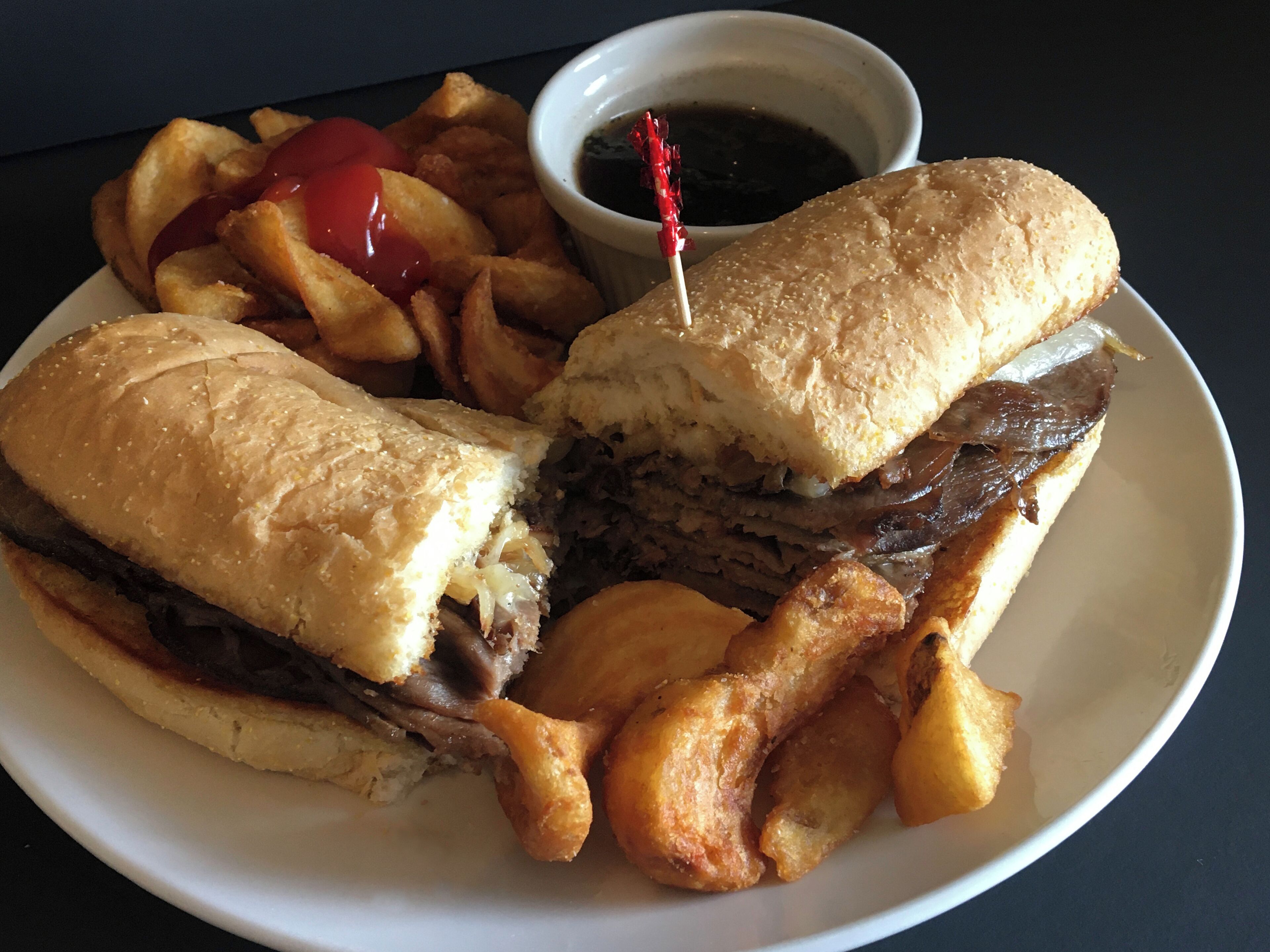 A plate with a sandwich, fries, and a small cup of sauce.