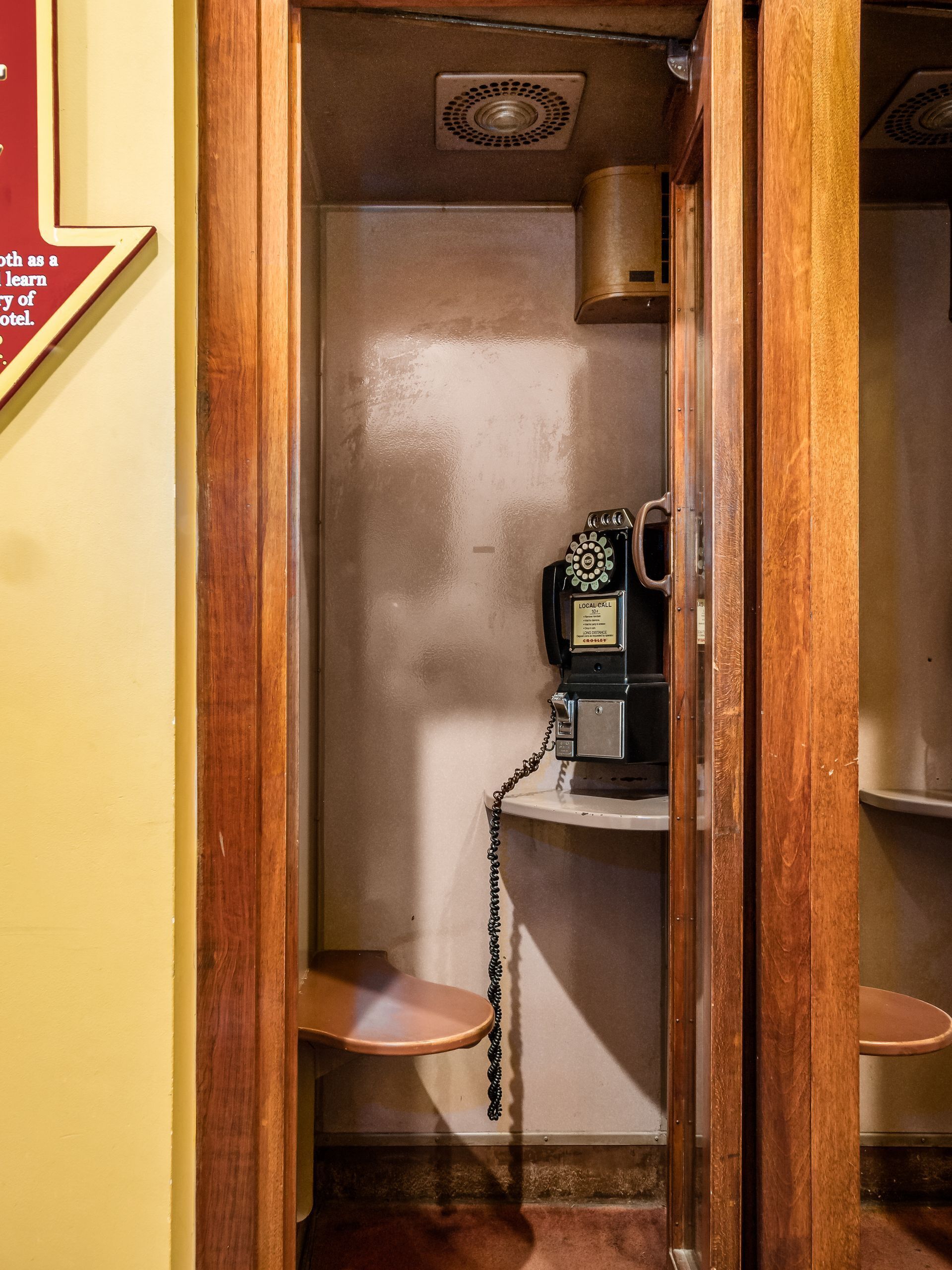 Um quarto estreito, com estrutura de madeira e um telefone antigo numa prateleira.