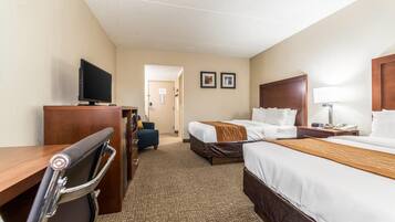 A hotel room with a desk, two beds, a TV, a chair, and a lamp.