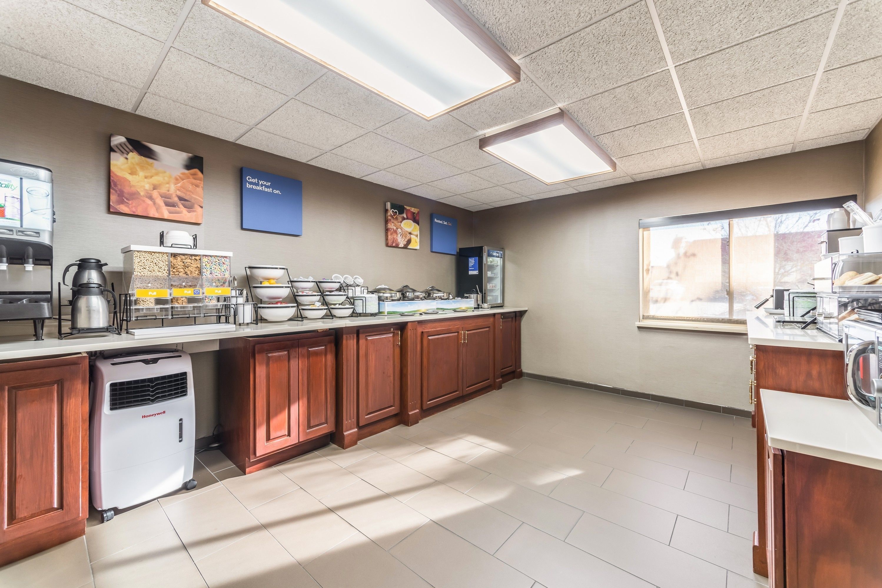 Un área de cocina bien iluminada con una estación de café, dispensadores de comida y un refrigerador.
