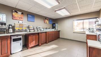 Un área de cocina bien iluminada con una estación de café, dispensadores de comida y un refrigerador.