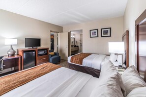 A hotel room with two beds, a desk with a television, a microwave, and a small kitchenette.