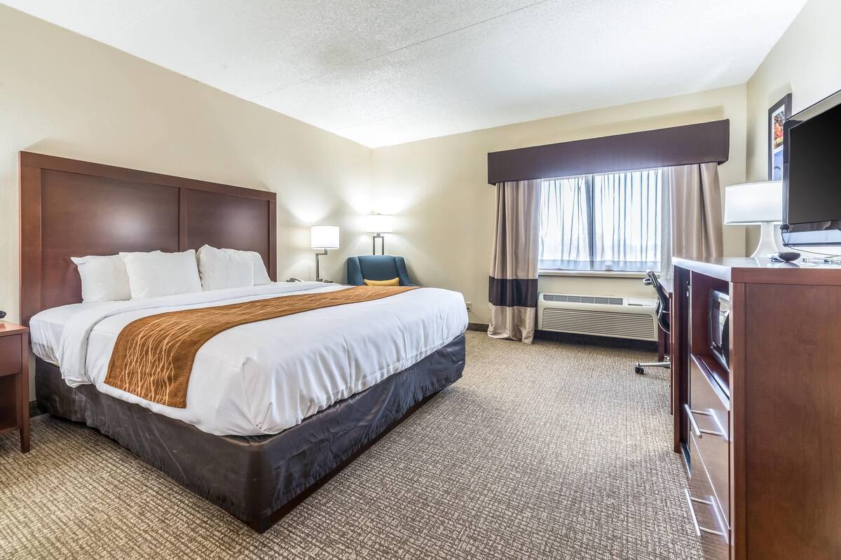 A hotel room with a large bed, a desk, a chair, a TV, and a window with curtains.