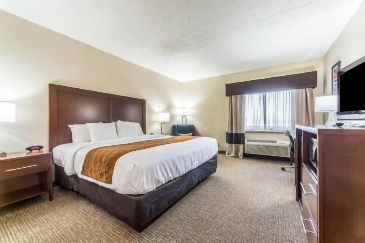 A hotel room with a bed, bedside tables, a desk with a chair, a television, and a window with curtains.