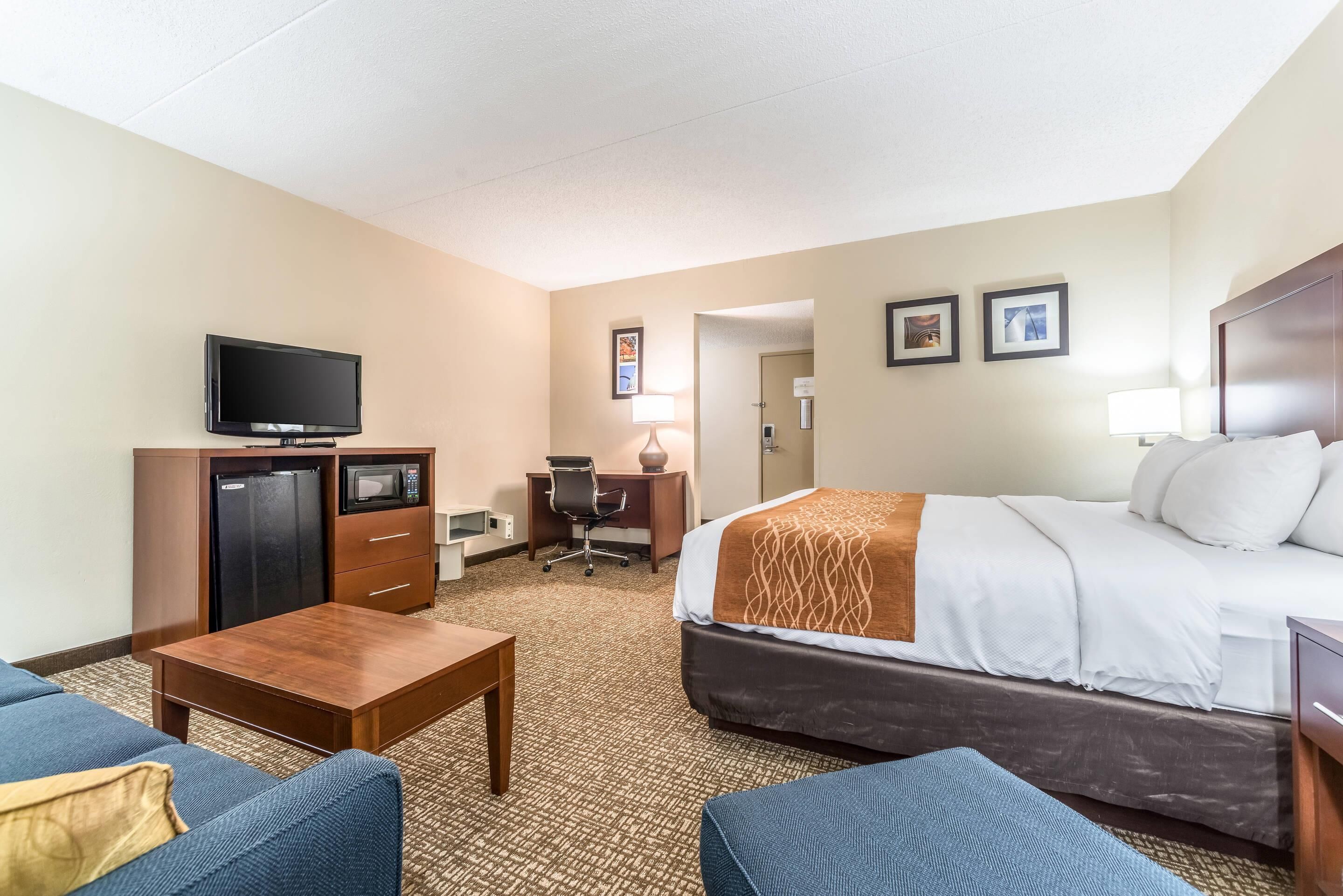 A hotel room with a bed, a desk, a television, a coffee table, and a couch.