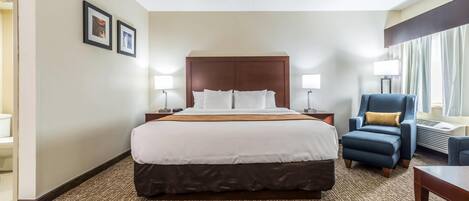 A hotel room with a large bed, two bedside tables, a chair, and a desk.