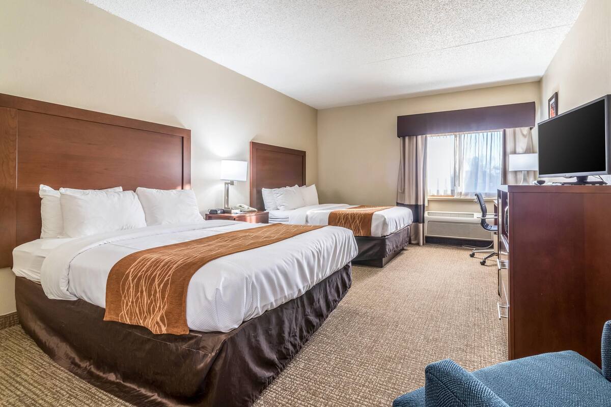 A hotel room with two beds, a desk, a television, and a view of the outdoors.