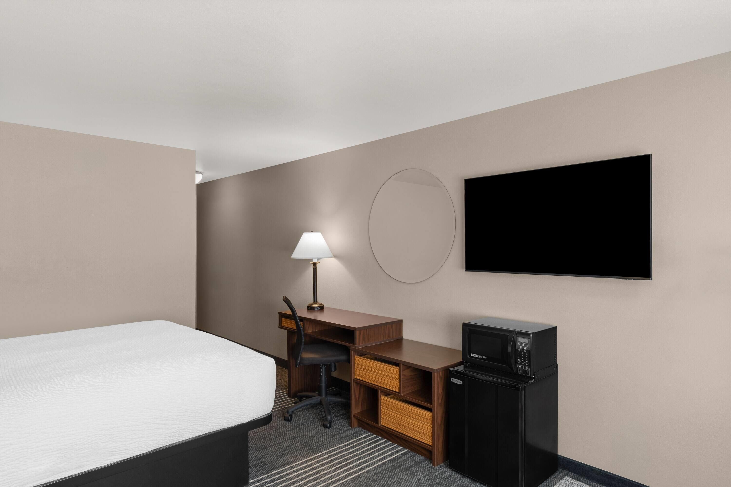 Ein Hotelzimmer mit Bett, Schreibtisch, Stuhl, Lampe, Fernseher und einer Mikrowelle.