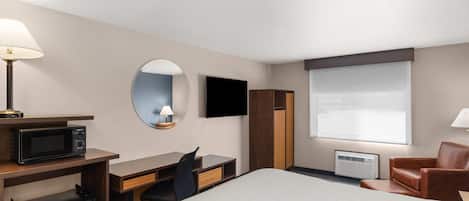 A hotel room with a bed, desk, chair, TV, and a small kitchenette.