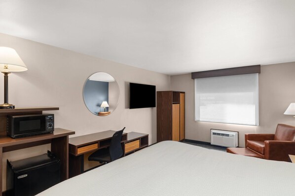 Habitación de hotel con cama, escritorio, silla, televisor y una pequeña kitchenette.
