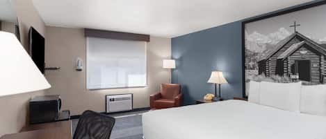 A hotel room with a bed, a desk, a chair, a lamp, a telephone, and a window.