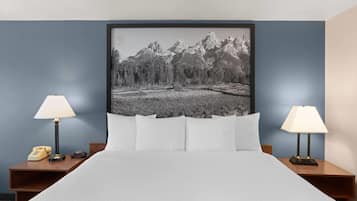Une chambre d’hôtel avec un lit, deux lampes de chevet, un téléphone et un tableau représentant un paysage de montagne.