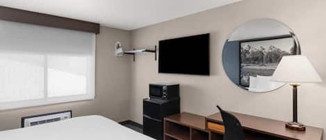 Quarto de hotel com cama, escrivaninha, cadeira, televisão e uma janela grande.