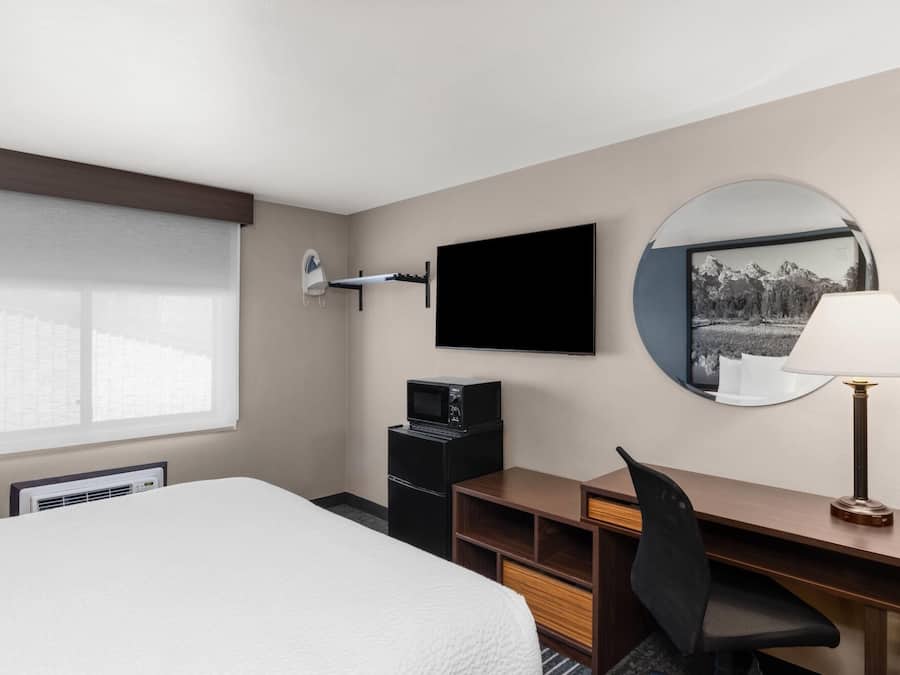 A hotel room with a bed, desk, chair, TV, and a large window.