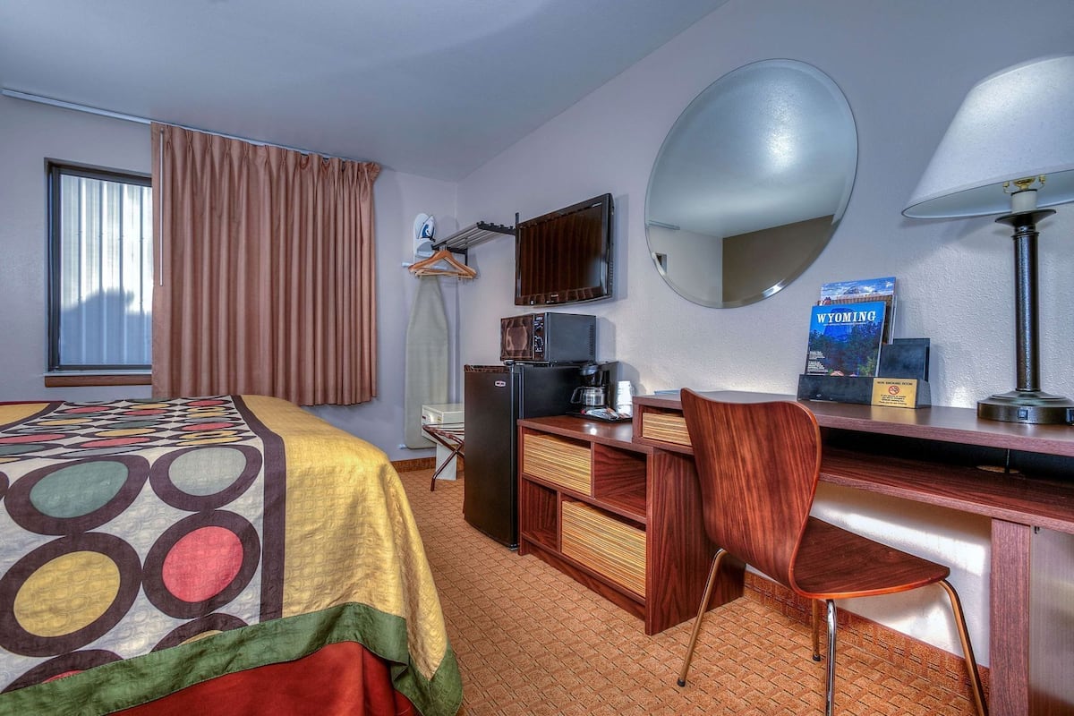 A hotel room with a bed, desk, chair, mirror, television, and a sign indicating a smoking room.
