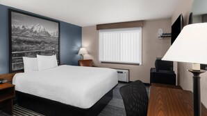 A hotel room with a large bed, a desk, a chair, a lamp, a TV, and a window with blinds. - Super 8 by Wyndham Jackson Hole (Jackson)