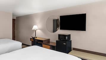 A hotel room with two beds, a desk with a lamp, a microwave, a flat-screen TV, and a mirror.