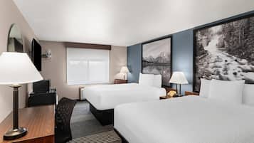 Habitación de hotel con dos camas, un escritorio, una silla, una lámpara de escritorio, un teléfono, un espejo y un cuadro grande con marco en la pared.