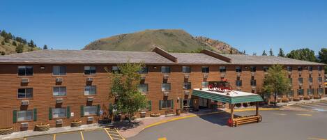 A multi-story hotel with a flat roof, a covered outdoor seating area, and a parking lot with marked handicapped spaces.