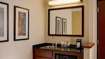 A hotel bathroom with a sink, mirror, framed artwork, and a coffee maker.