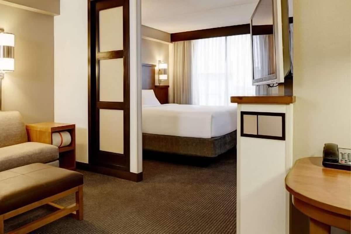 A hotel room with a sofa, a small table, a bed, a TV, and a desk with a phone.